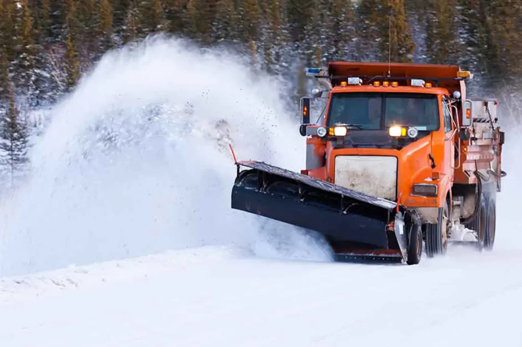 Commercial snow plow truck clearing heavy snow from a roadway during winter storm conditions.